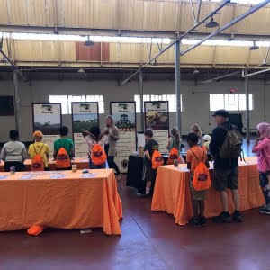 People attending an indoor community event with informational booths and orange tablecloths.